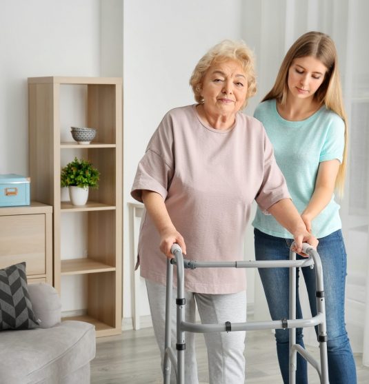Young woman and her elderly grandmother with walking frame at home